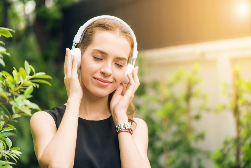 Smiling woman listening to music with headphones in sunny garden setting.