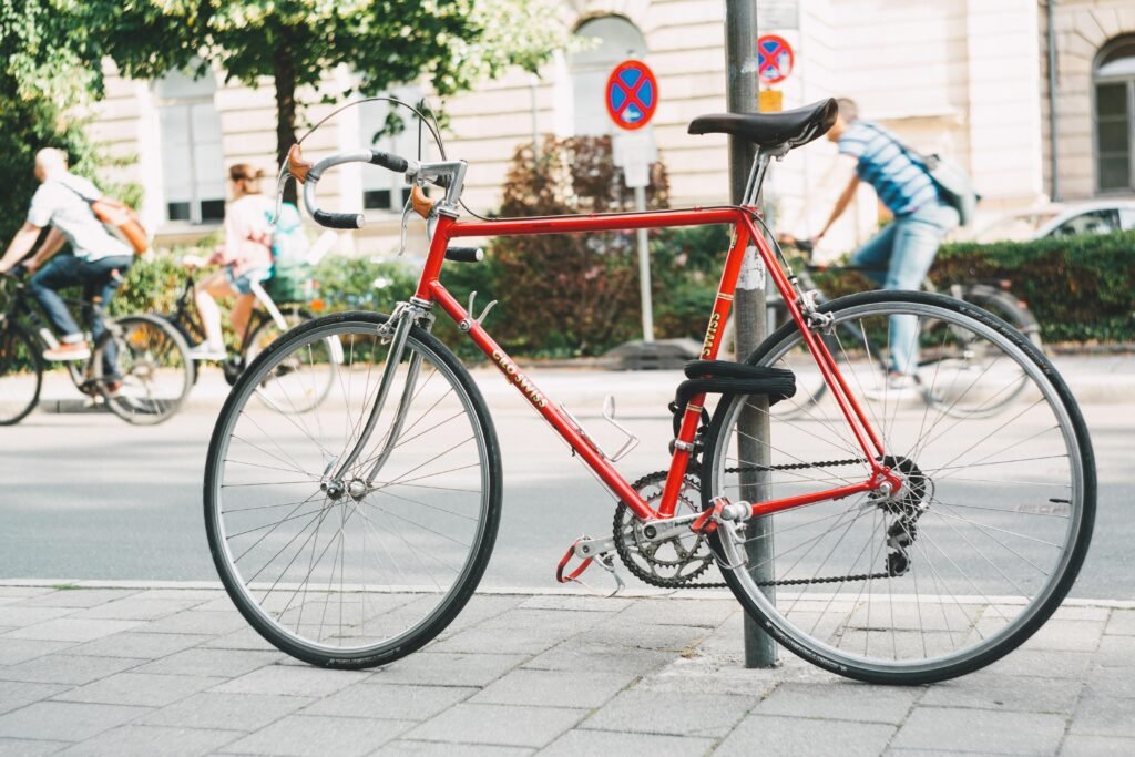 Red bike locked to pole on paved street with cyclists in background, perfect for urban travel theme.