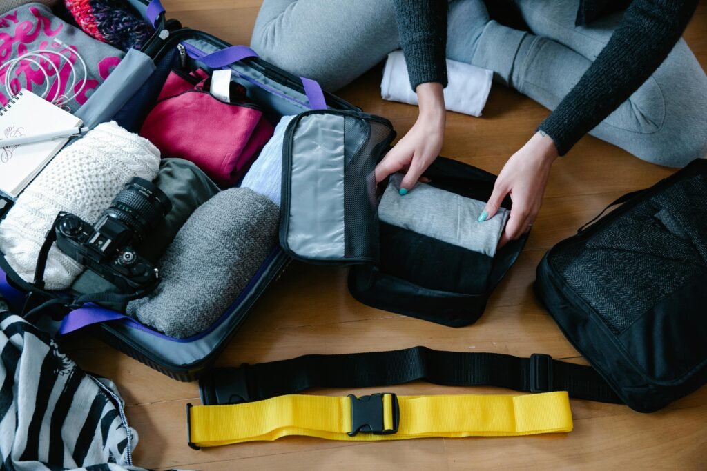 A woman arranging clothes and accessories into a suitcase, preparing for travel.